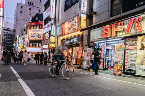 A man rides a bicycle through a busy Japanese street.
